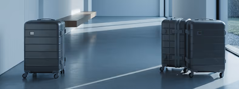 Three black rolling suitcases standing on a shiny blue floor inside a modern room with large windows.